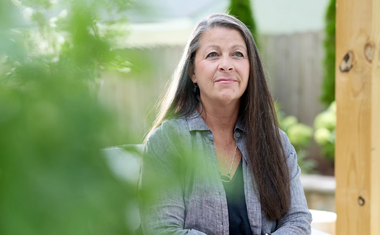 A woman sitting outdoors in her garden, looking ahead thoughtfully